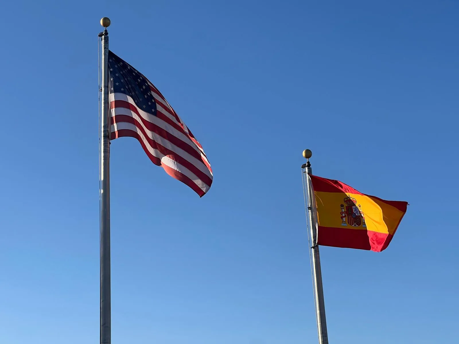 US and Spanish flags against a blue sky