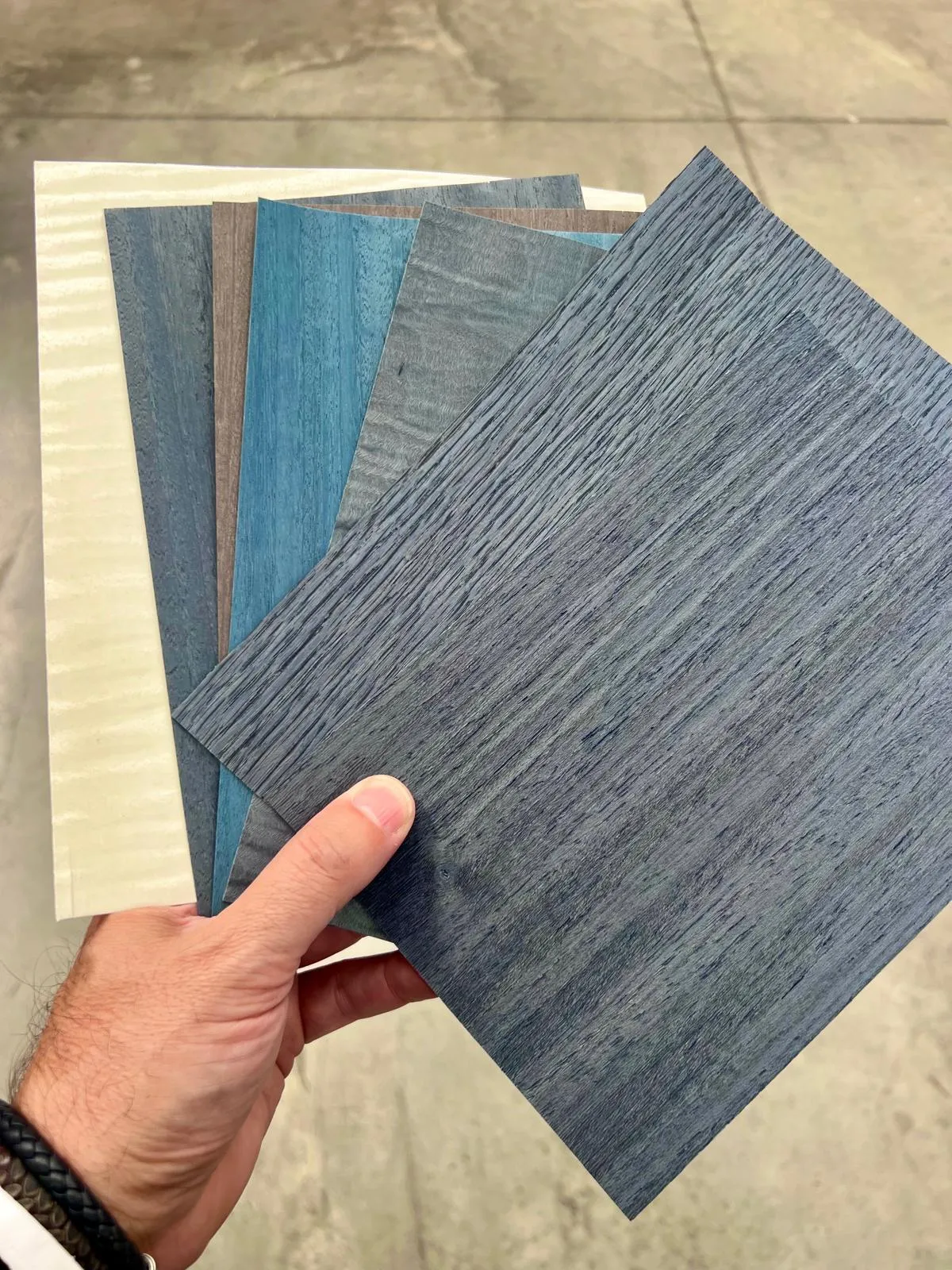 Hand holding dyed veneer samples in blue and grey tones