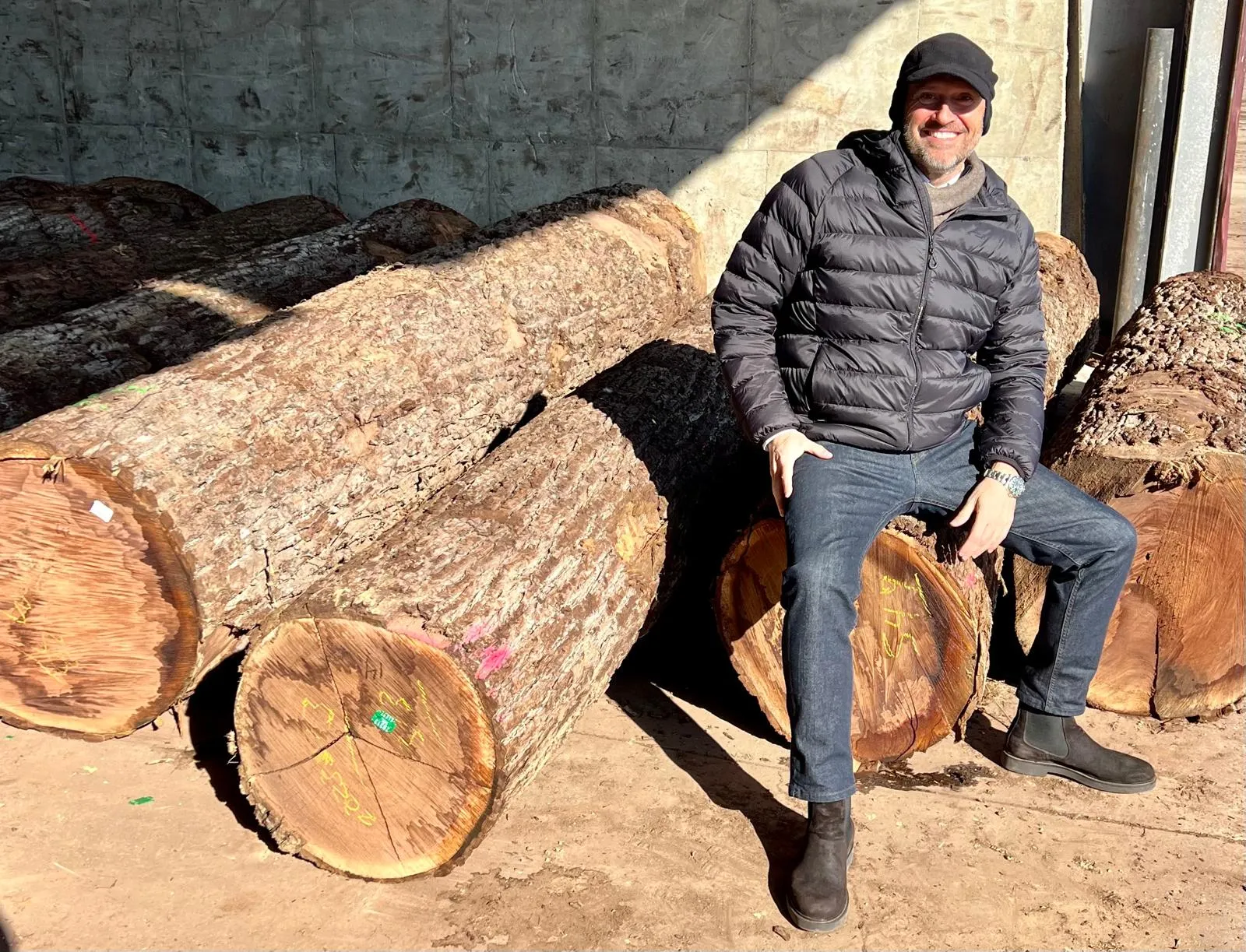 Pablo Ferraro sitting on hardwood logs at a timber yard